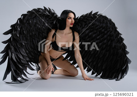 Woman in black lingerie poses gracefully with dramatic black wings Woman in black lingerie poses gracefully with dramatic black wings 125690321
