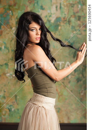 Healthy brunette woman wearing fashionable dress on green painted background indoor Healthy brunette woman wearing fashionable dress on green painted background indoor 125690454