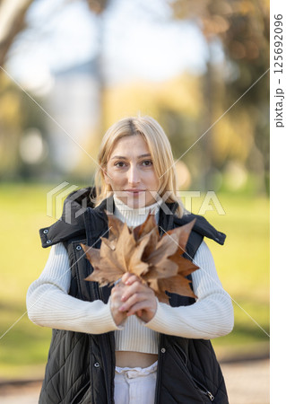 Young woman holding dry leaves in autumn park 125692096