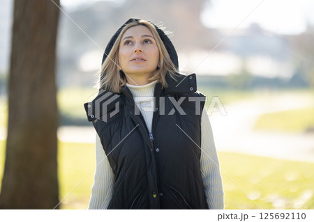 Woman wearing vest and looking up in a park during a sunny day 125692110