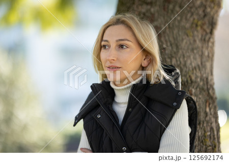 Blond woman leaning against tree enjoying day in park Blond woman leaning against tree enjoying day in park 125692174