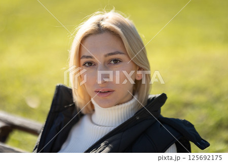 Portrait of a blonde woman sitting on a bench, enjoying a sunny day in a park 125692175