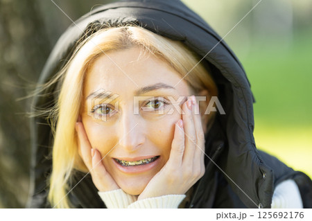 Blonde woman wearing braces and holding her face with hands Blonde woman wearing braces and holding her face with hands 125692176