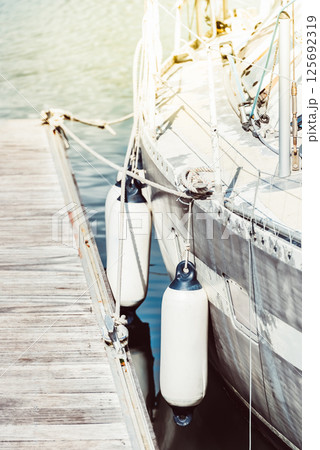 Sailboat docked at marina with sunlight, water reflection, wooden pier background Sailboat docked at marina with sunlight, water reflection, wooden pier background 125692319