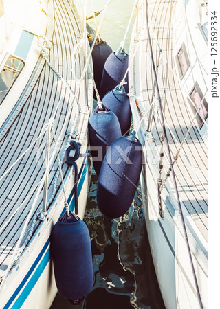 Sailboats with protective fenders anchored at marina, sunlight creating reflections 125692334