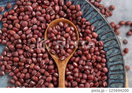 Blue plate full of dried red azuki beans with a wooden spoon top view. Vegetarian protein source Blue plate full of dried red azuki beans with a wooden spoon top view. Vegetarian protein source 125694200