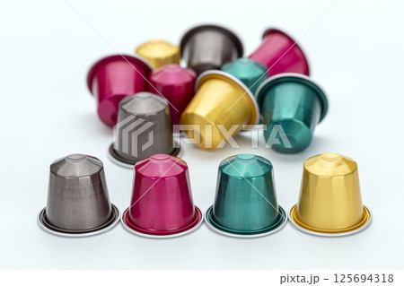 Colorful coffee capsules scattered on white background, featuring vibrant hues of pink, gold, teal, and silver. arrangement creates lively and inviting atmosphere 125694318