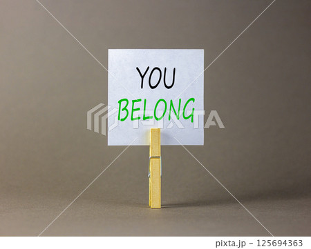 Belonging and you belong symbol. Concept words You belong on beautiful white paper on wooden clothespin. Beautiful grey background. Business belonging and you belong concept. Copy space. 125694363