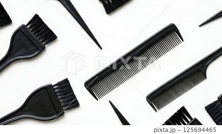 Flat lay of professional black hairdressing tools including combs and dye brushes arranged on a white background. 125694465