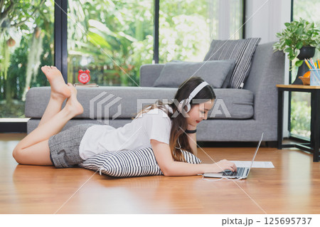 Pretty young woman wear headphones lying down on floor and usinging laptop. Distance learning. Remote work place. Quarantine, coronovirus pandemic covid-19. Pretty young woman wear headphones lying down on floor and usinging laptop. Distance learning. Remote work place. Quarantine, coronovirus pandemic covid-19. 125695737
