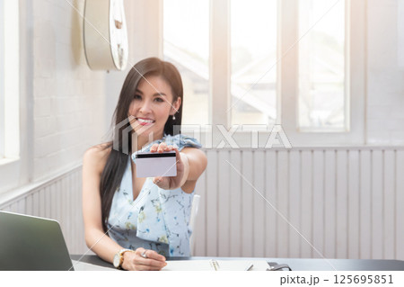 Smiling beautiful Asian woman presenting credit card in hand showing trust and confidence for making payment. Online shopping concept. 125695851