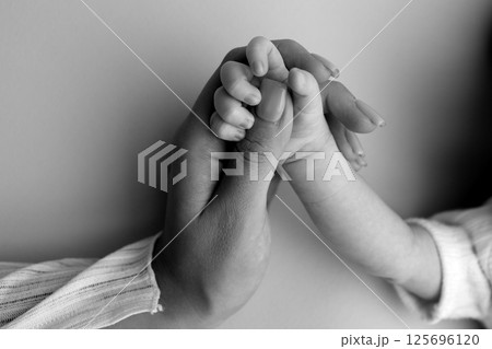 Close-up little hand of child and palm of mother and father. The newborn baby has a firm grip on the parent's finger after birth. A newborn holds on to mom's, dad's finger. Black and white photo. Close-up little hand of child and palm of mother and father. The newborn baby has a firm grip on the parent's finger after birth. A newborn holds on to mom's, dad's finger. Black and white photo. 125696120