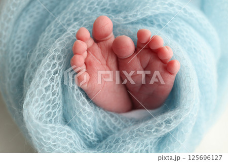 Baby foot on blue soft coverlet, blanket. Close-up of tiny, cute, bare toes, heels and feet of a newborn girl, boy.  125696127