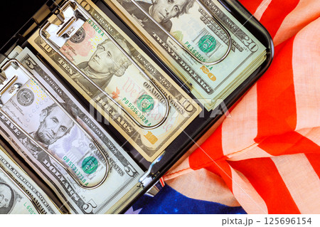 Dollars cash with U.S. filled briefcase resting an American flag symbolizing wealth patriotism in business setting 125696154