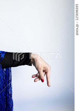 Female hand gesture with blue fabric and red nails against light background 125696895