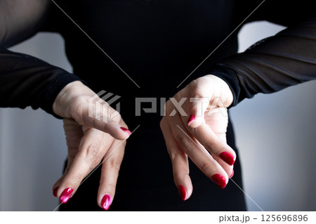 Caucasian female hands with red nails in artistic pose wearing black long sleeve attire Caucasian female hands with red nails in artistic pose wearing black long sleeve attire 125696896