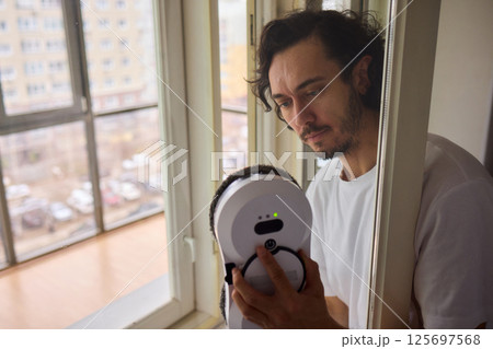 A man uses a robotic vacuum cleaner to assist with cleaning tasks in his home environment A man uses a robotic vacuum cleaner to assist with cleaning tasks in his home environment 125697568