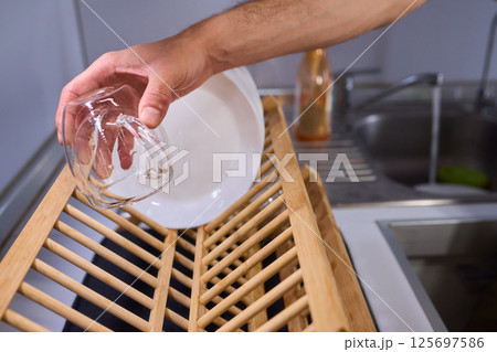Carefully hand placing a clean, sparkling dish into the drying rack for organization and hygiene Carefully hand placing a clean, sparkling dish into the drying rack for organization and hygiene 125697586