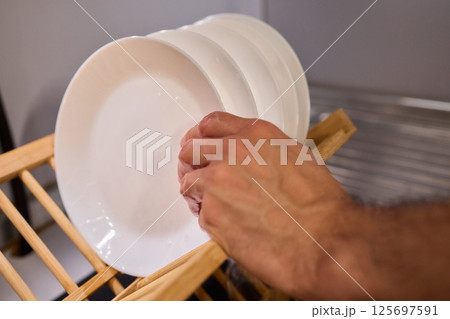 Carefully hand placing a clean, sparkling dish into the drying rack for organization and hygiene Carefully hand placing a clean, sparkling dish into the drying rack for organization and hygiene 125697591