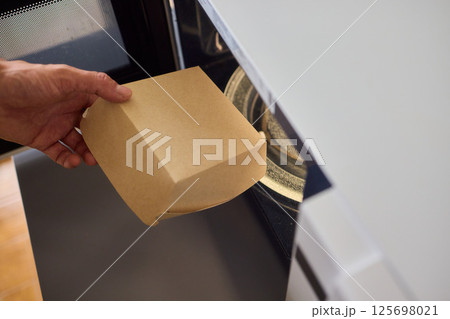 Hand delicately placing a takeout container into the microwave to warm up the meal Hand delicately placing a takeout container into the microwave to warm up the meal 125698021