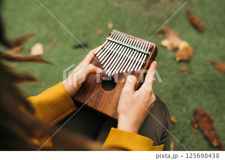 close-up woman playing the musical instrument Kalimba or Mbira in the fall on the terrace close-up woman playing the musical instrument Kalimba or Mbira in the fall on the terrace 125698438