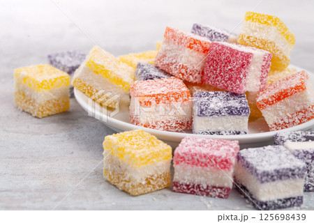 Cubes of multi-colored marmalade in powdered sugar on plate. The concept of baby sweets. Cubes of multi-colored marmalade in powdered sugar on plate. The concept of baby sweets. 125698439