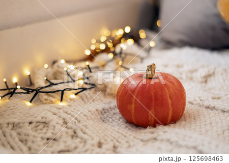 Autumn still life. Pumpkin on white knitted plaid with garland - halloween home decor, concept of fall season, Warm, hygge, cozy, rustic style home decor, copy space, banner Autumn still life. Pumpkin on white knitted plaid with garland - halloween home decor, concept of fall season, Warm, hygge, cozy, rustic style home decor, copy space, banner 125698463