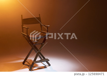 The director's chair stands in a beam of light with an orange backlight and smoke. Place for text. Free chair. Concept of selection and casting. Shadow and light. 125698471