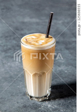 Iced coffee in a tall glass with cream or milk and straw on gray background with copy space Iced coffee in a tall glass with cream or milk and straw on gray background with copy space 125698555