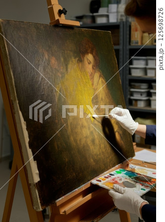 Art restorer cleaning painting with cotton swab in restoration studio 125698726