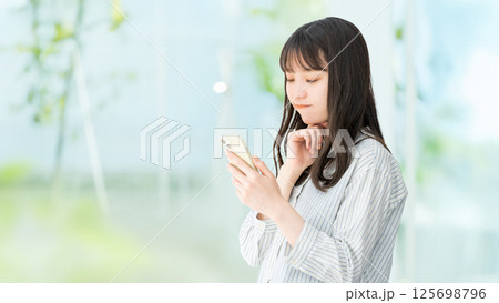 スマートフォンを見て考える女性・ビジネスウーマン スマートフォンを見て考える女性・ビジネスウーマン 125698796