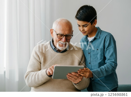Grandfather and grandson using digital tablet together at home, bonding over technology Grandfather and grandson using digital tablet together at home, bonding over technology 125698861