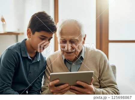Grandfather and grandson using digital tablet together at home, bonding over technology 125698867