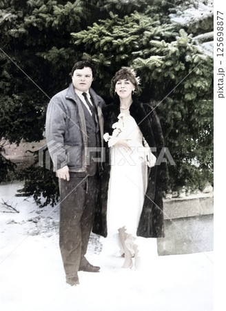 Vintage portrait of the bride and groom in a snowfall against the background of snow-covered fir trees. Retro photo from 1993. Vintage portrait of the bride and groom in a snowfall against the background of snow-covered fir trees. Retro photo from 1993. 125698877