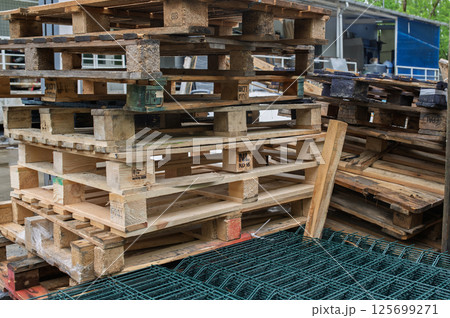 Stacked wooden pallets near metal fence creating industrial scene 125699271