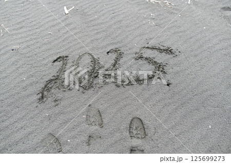 2025 written on wet sand with footprints nearby, concept of new year and future 125699273