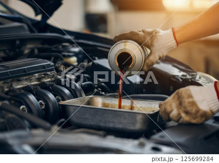 Mechanic pouring oil into car engine for maintenance service Mechanic pouring oil into car engine for maintenance service 125699284