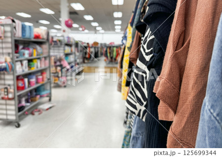 A clothing store aisle shows racks filled with various colorful garments and nearby shelves stocked with miscellaneous retail products 125699344