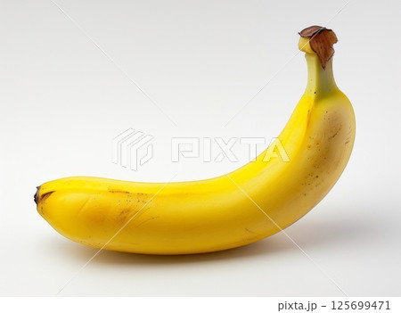 A single, ripe yellow banana with a slightly bruised stem sits on a plain white background 125699471