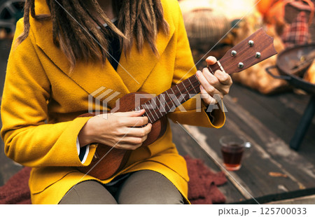 girl with dreadlocks closeup playing an acoustic instrument ukulele in autumn on the terrace 125700033