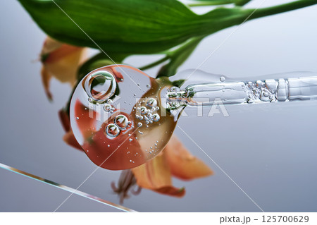 A pipette with a beautiful drop of serum on a background of lily flowers. 125700629