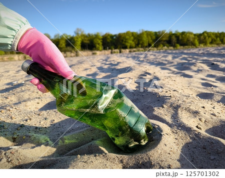 Closeup of volunteer hand in pink gloves putting plastic bottle inside plastic bag on the sand. A volunteer picks up a plastic bottle on the beach. Closeup of volunteer hand in pink gloves putting plastic bottle inside plastic bag on the sand. A volunteer picks up a plastic bottle on the beach. 125701302