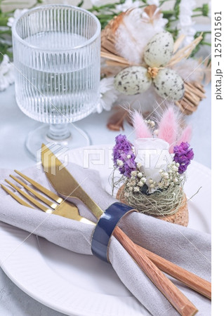Easter table setting decorated with flower arrangement and golden cutlery, vertical 125701561