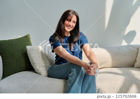 Portrait of beautiful young brunette woman sitting on sofa in living room Portrait of beautiful young brunette woman sitting on sofa in living room 125702606