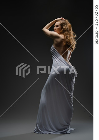 Sensual portrait of a woman elegantly draped in soft fabric at dusk 125702765