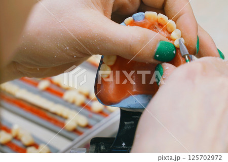 Expert dental technician skillfully shaping dentures in laboratory setting Expert dental technician skillfully shaping dentures in laboratory setting 125702972
