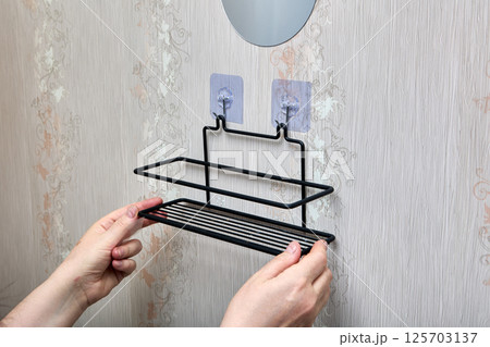 Wire bathroom shelf is being hooked onto two transparent nano adhesive hooks on wall offering quick and tool-free installation for bathroom storage. 125703137