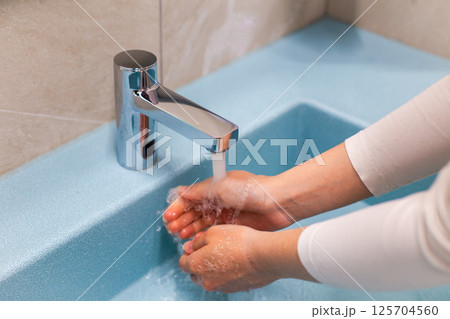washing hands under running water at the sink in the bathroom 125704560
