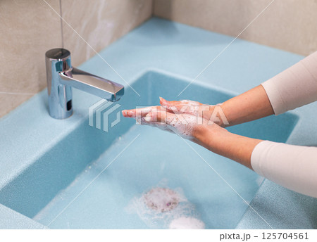 Person washing hands with soap and water in a blue sink Person washing hands with soap and water in a blue sink 125704561