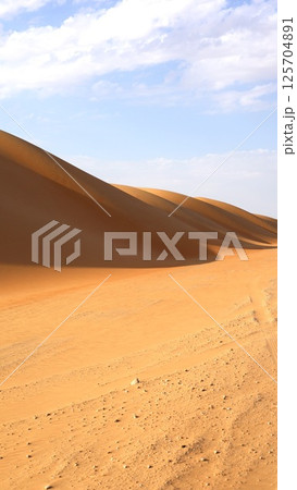 Sharp dune wall rises steep and smooth, edge cuts through glowing horizon as morning light draws golden line across untouched sand, surreal beauty forms minimalist tourist attraction. Sharp dune wall rises steep and smooth, edge cuts through glowing horizon as morning light draws golden line across untouched sand, surreal beauty forms minimalist tourist attraction. 125704891